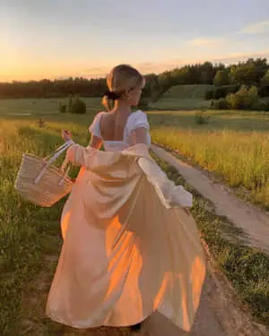A confident young woman standing against a sunset background.