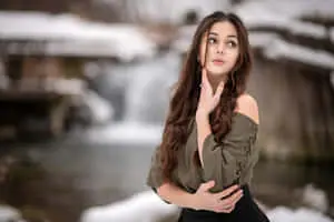 a young woman standing in the snow near a waterfall