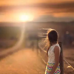 a girl standing on a dirt road at sunset