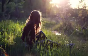 a girl sitting in the grass at sunset